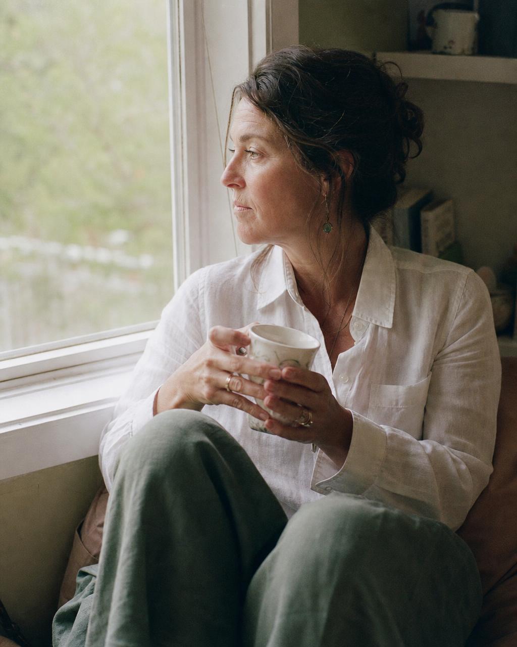 A woman sitting by a window with a cup of tea, quietly reflecting