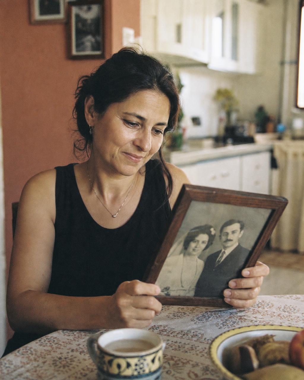 An adult daughter at her kitchen table holding an old family photograph